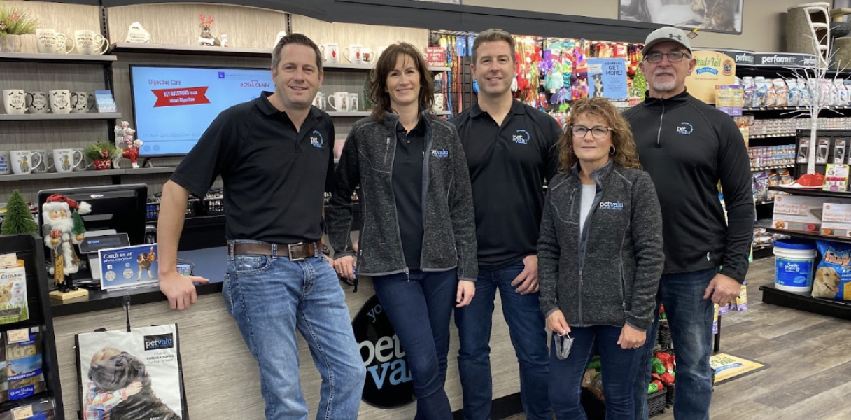 Five animal care experts wearing Pet Valu shirts stand in front of a checkout at a Pet Valu store