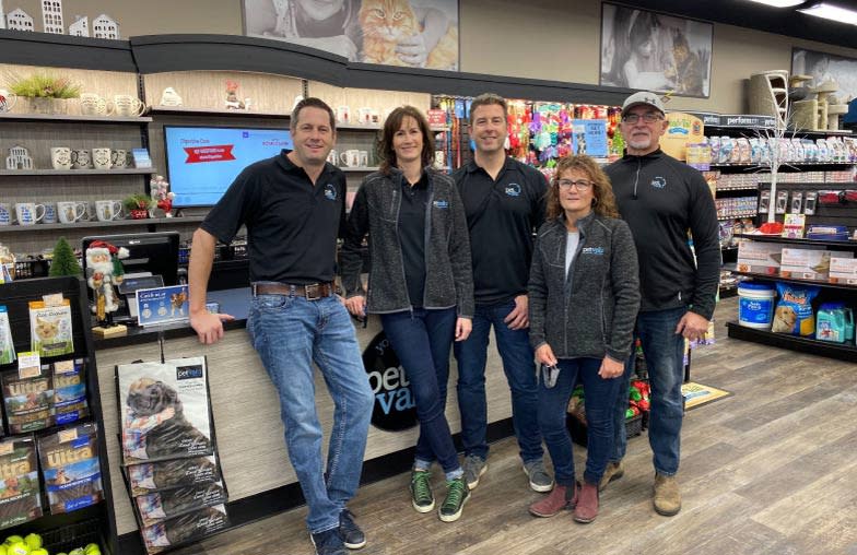 Five animal care experts wearing Pet Valu shirts stand in front of a checkout at a Pet Valu store