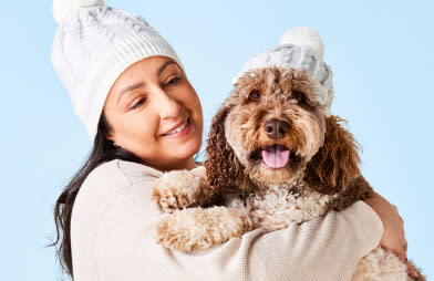 a woman holding a dog wearing winter clothes