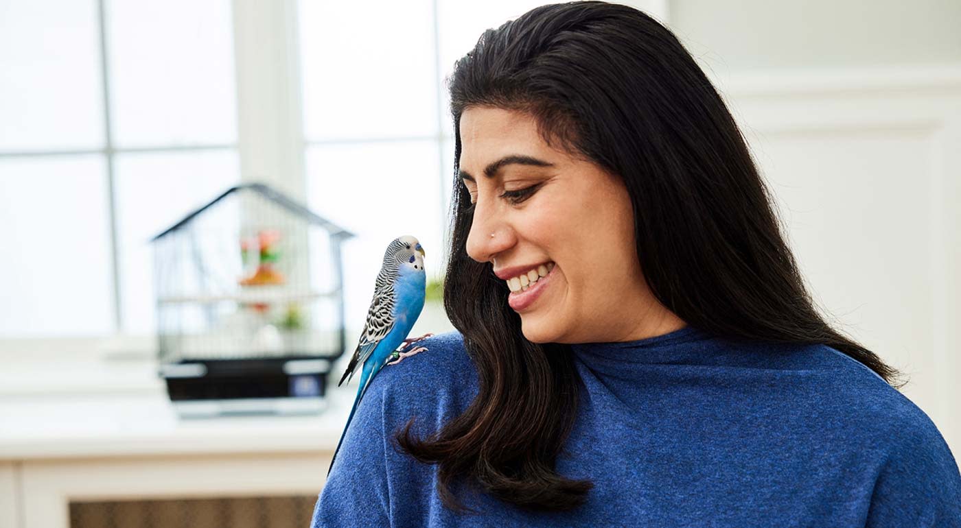 Woman smiling at a bird sitting on her shoulder