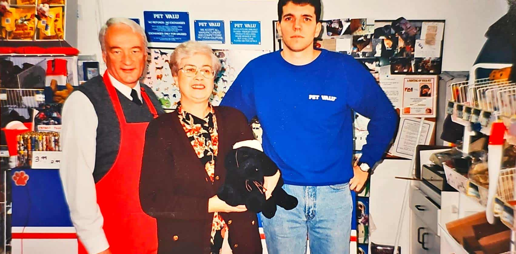 A son and his father, as well as his mother holding a dog, stand in a Pet Valu store backroom