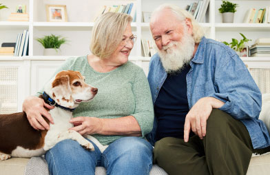 Happy senior man and woman sitting on their couch with their pet dog and sharing a laugh