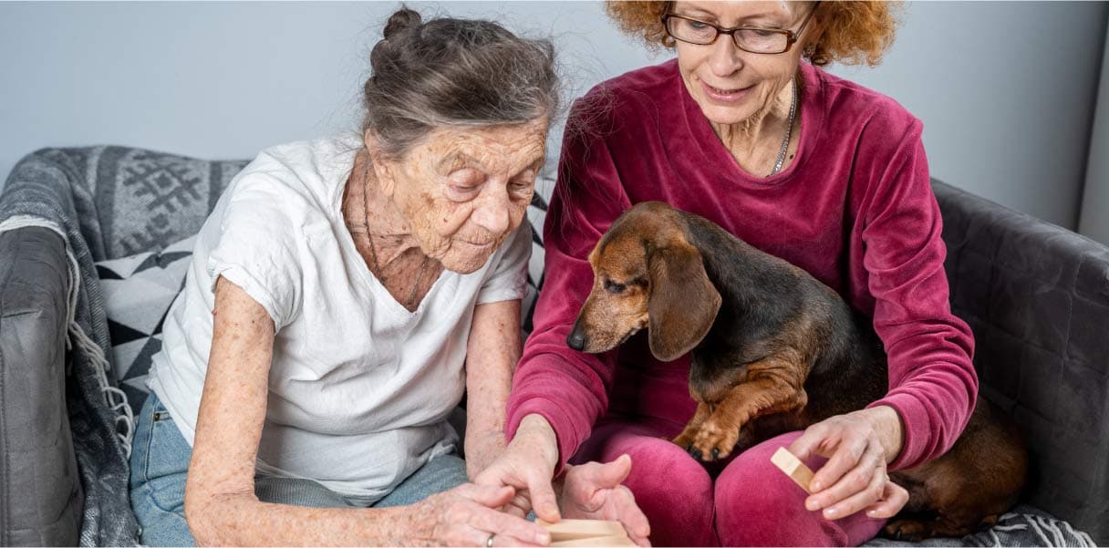 Daughter and older mother play a game on the couch with the family dog