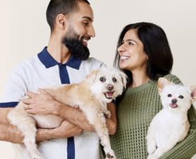 A young man and woman hold a friendly, medium tan dog and a small white dog and pose for a photo