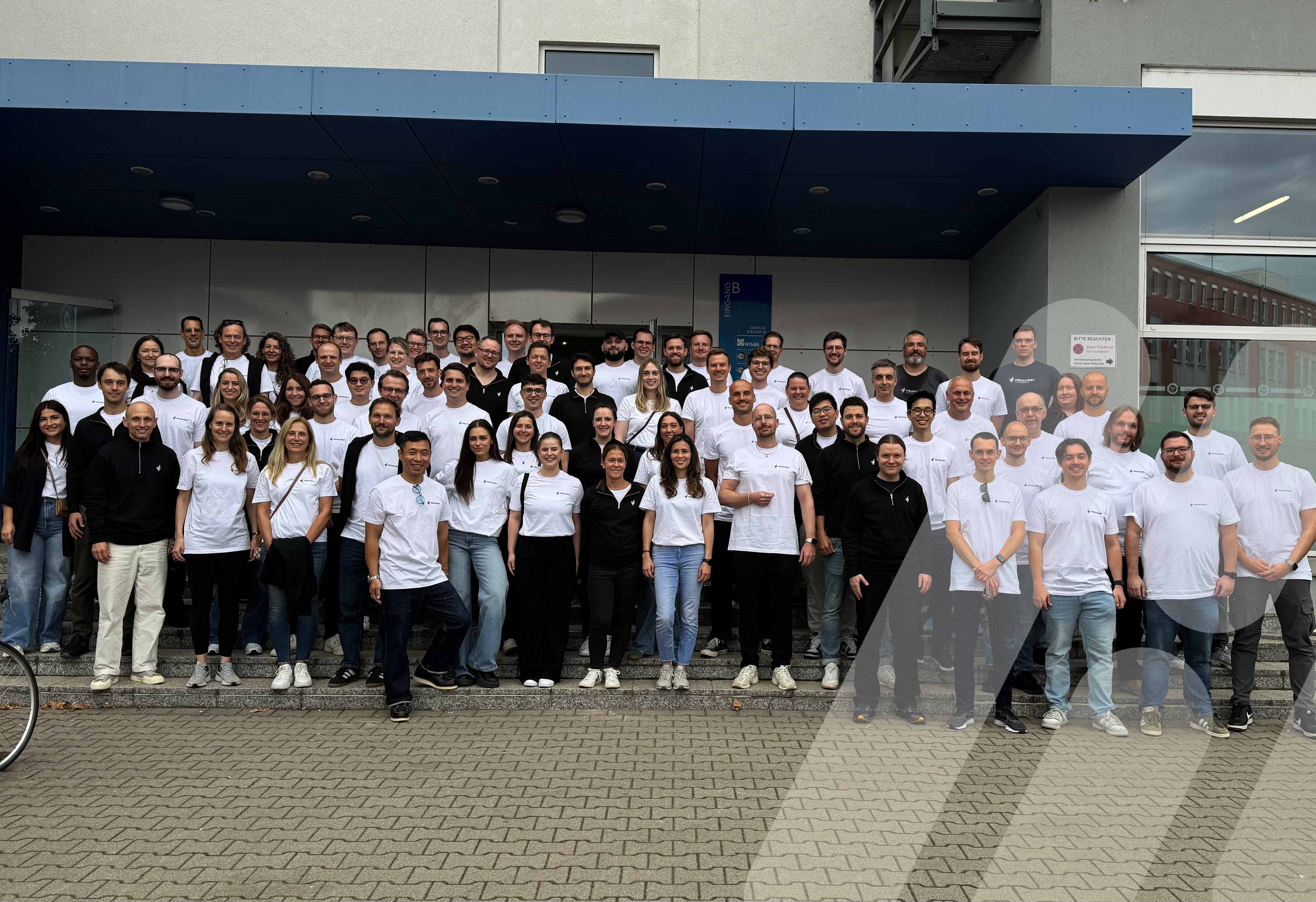 Großes Teamfoto vor einem Bürogebäude, viele Personen in weißen T-Shirts.