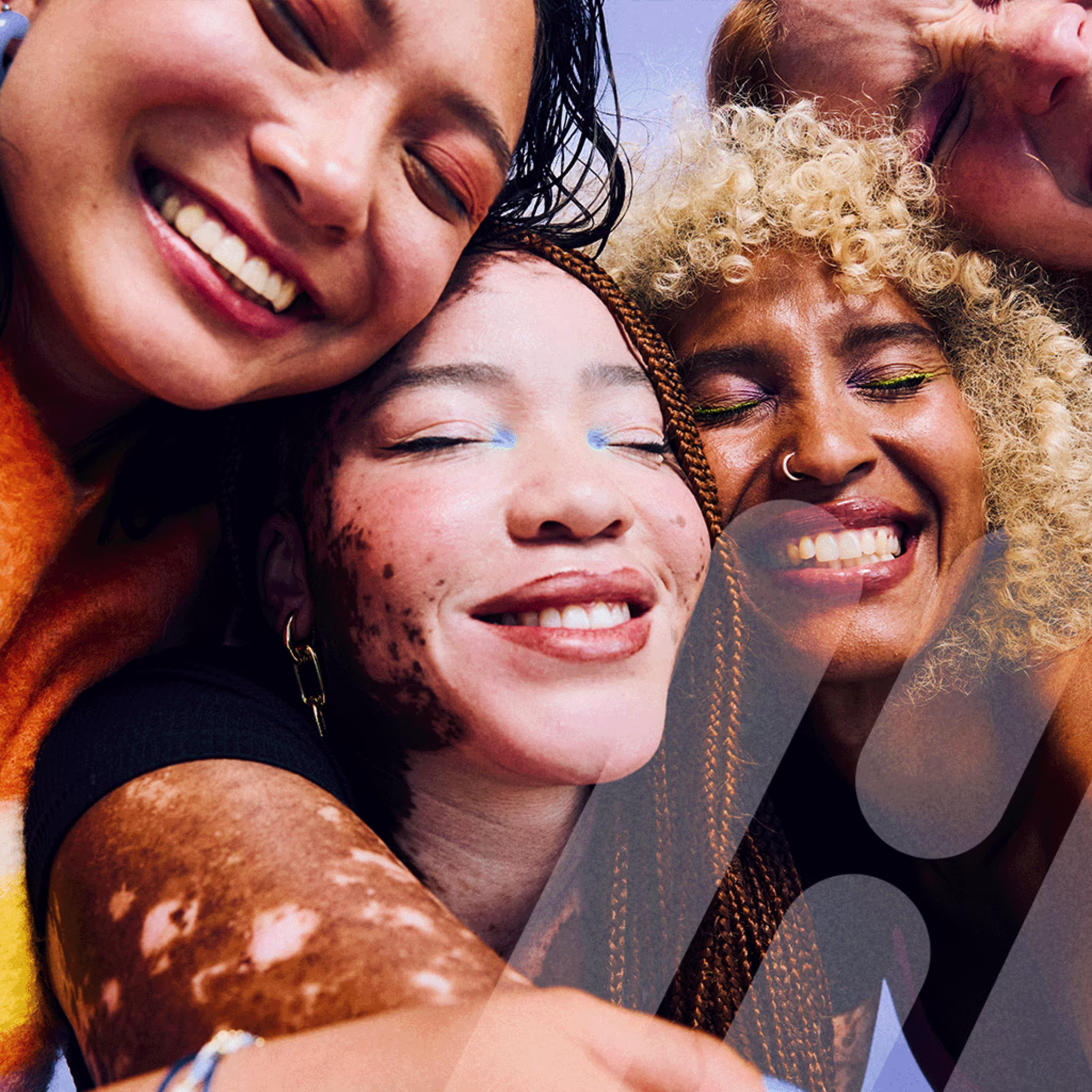 Vier Frauen mit geschlossenen Augen lachen herzlich und lehnen die Köpfe eng aneinander. Sie tragen farbenfrohes Make-up und Kleidung, die ihre Individualität unterstreichen. Das Bild strahlt Freude, Zusammenhalt und Vielfalt aus.