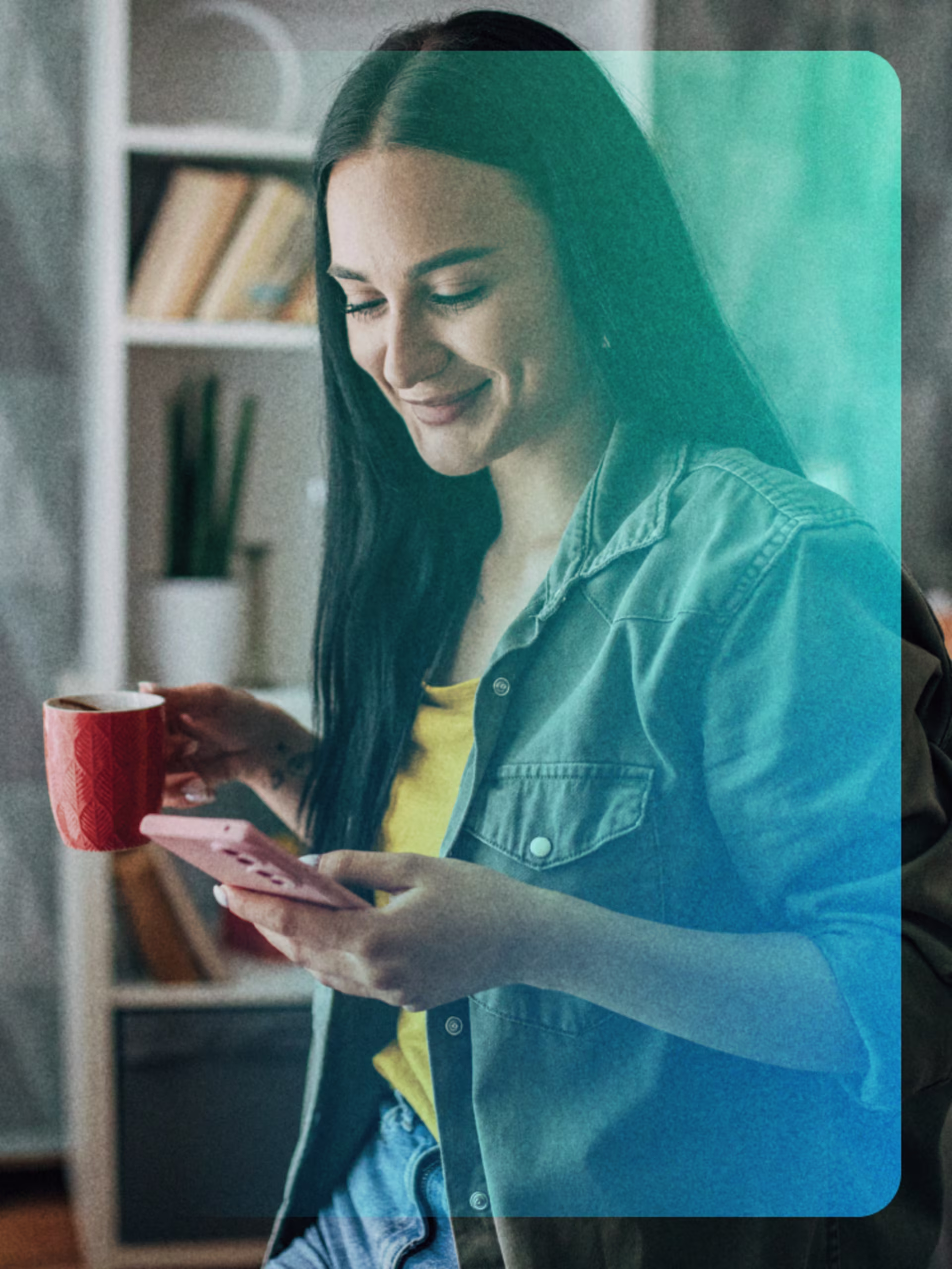 Frau mit Tasse schaut lächelnd auf ihr Smartphone, im gemütlich eingerichteten Wohnzimmer.