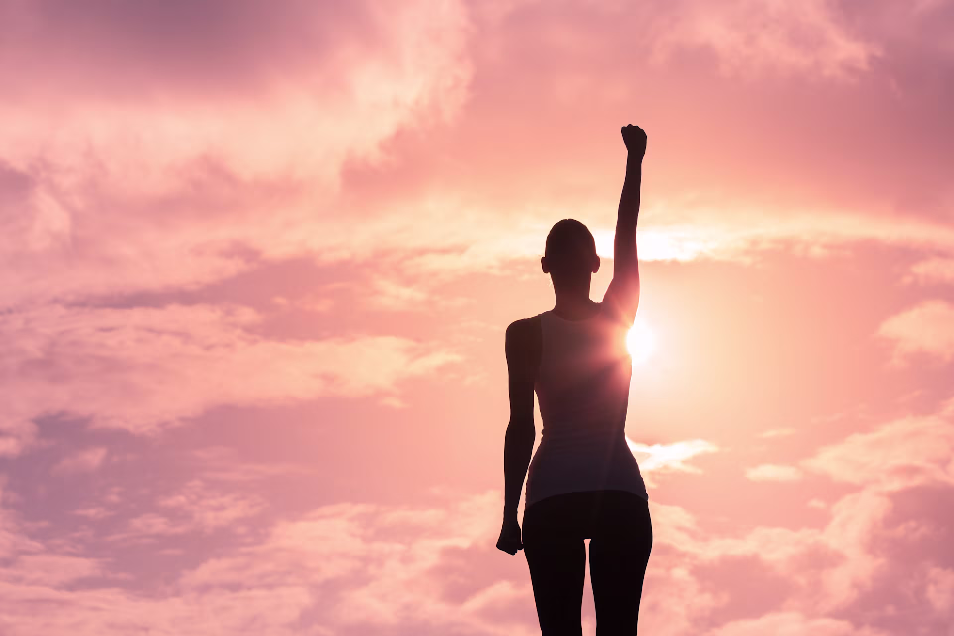 Frau im Sonnenuntergang streckt ihre Faust in den Himmel