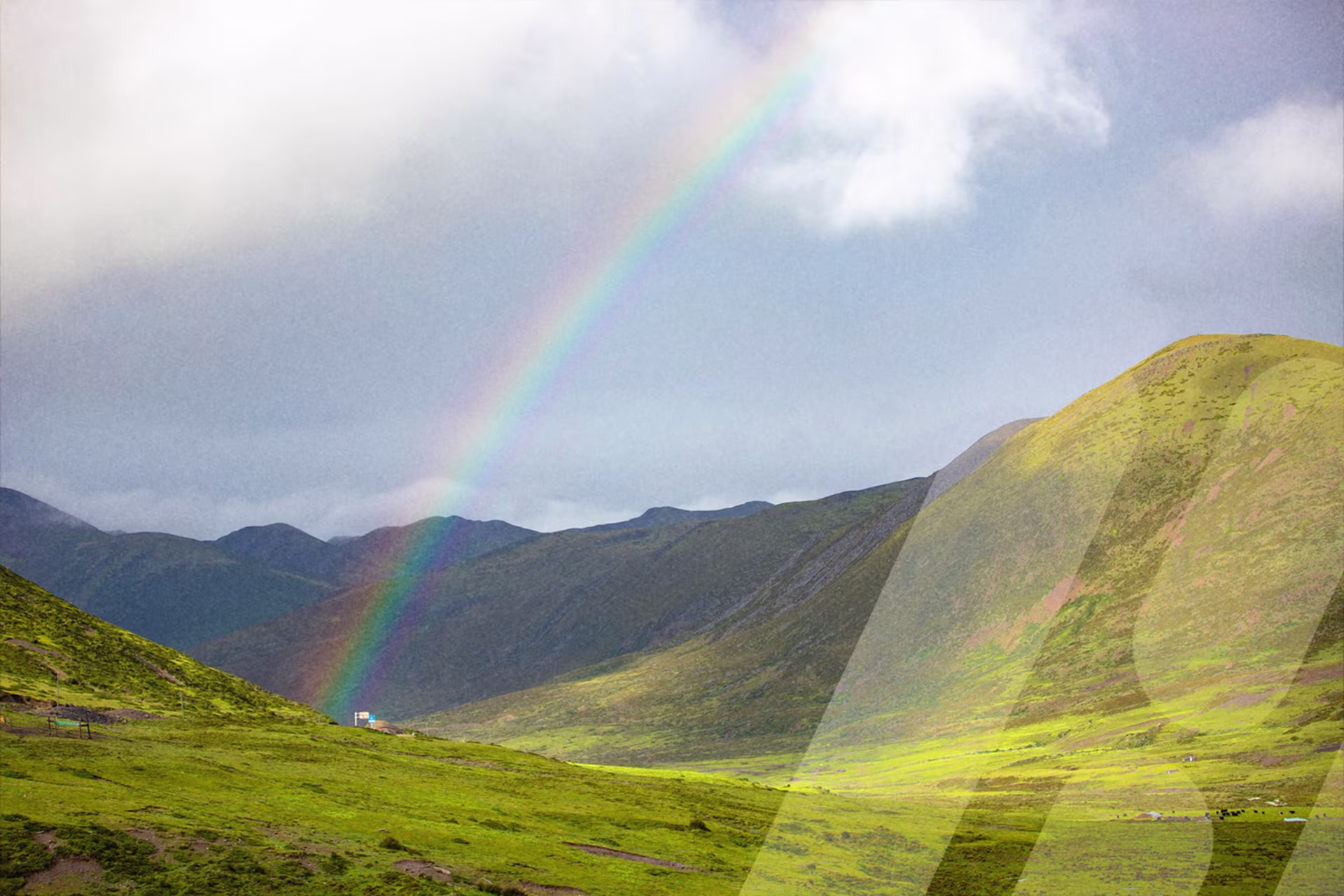 Regenbogen über einer grünen Berglandschaft.