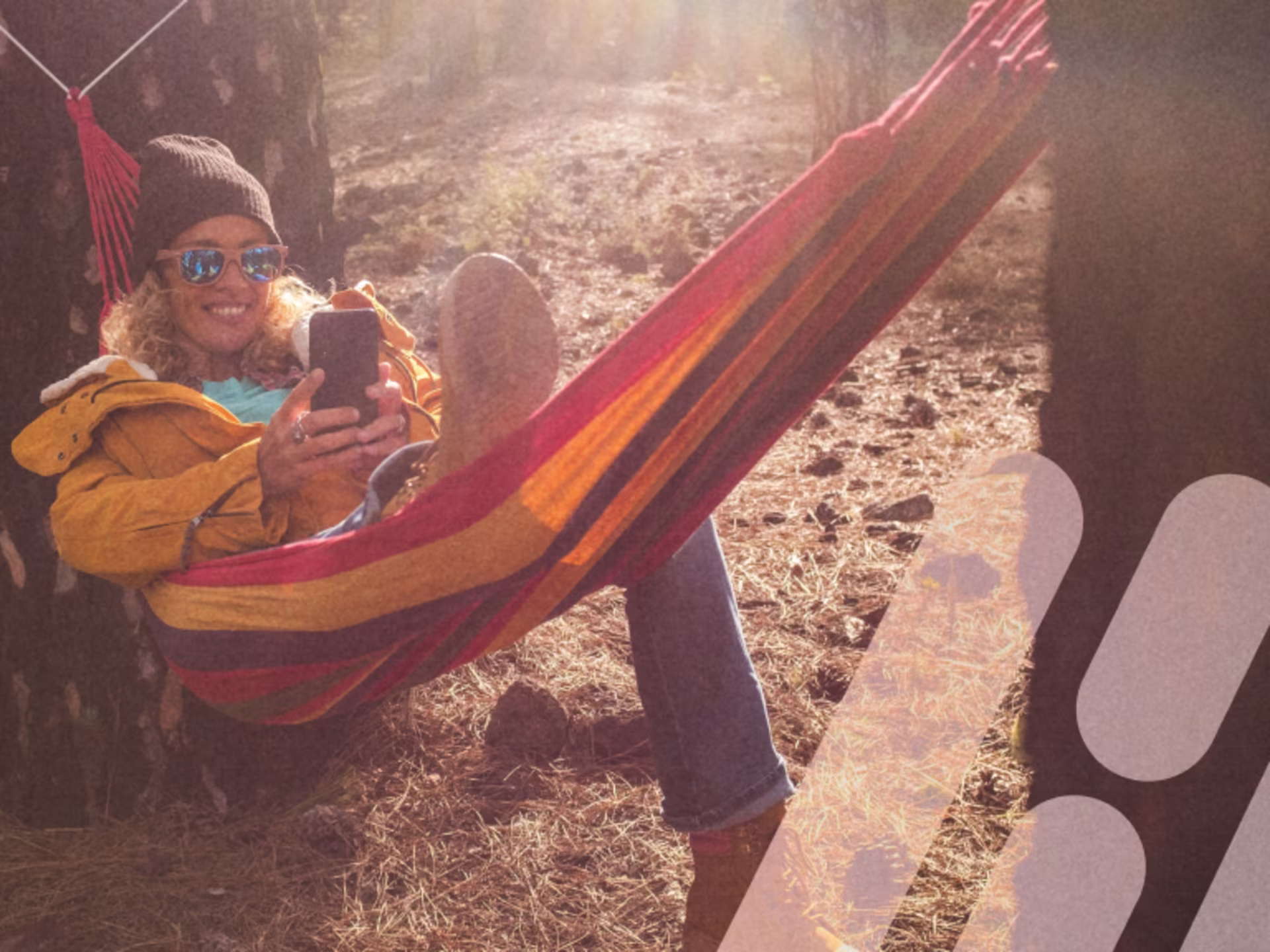 Frau liegt entspannt in einer Hängematte und schaut lächelnd auf ihr Smartphone.