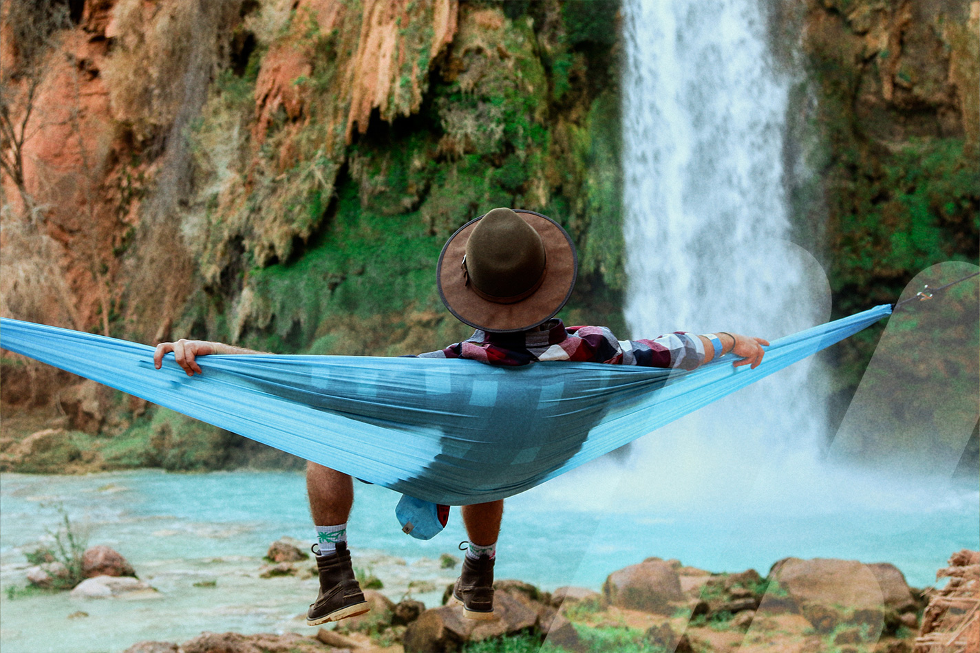Person entspannt in einer Hängematte vor einem Wasserfall.