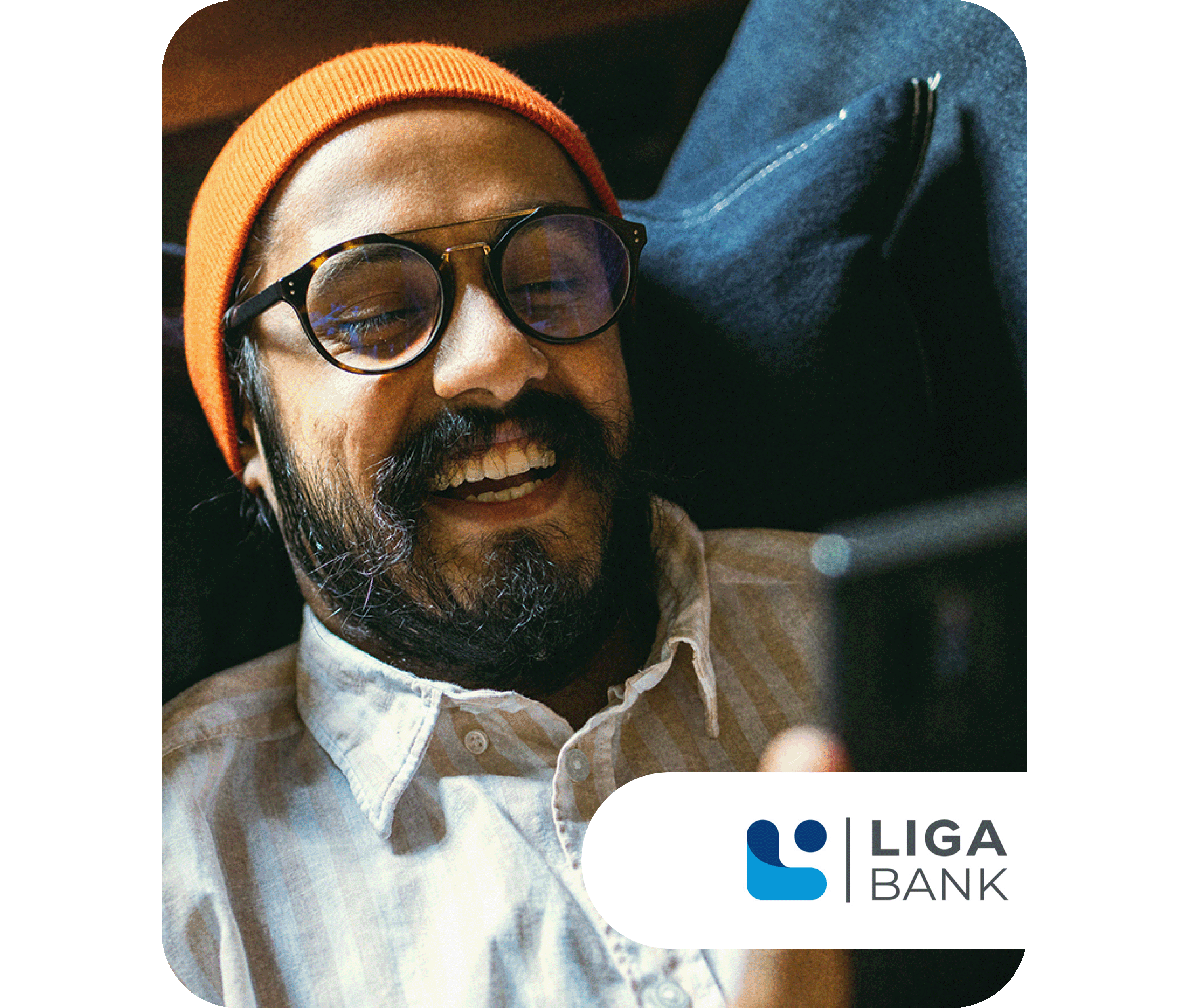 Lächelnder Mann mit Brille und orangefarbener Mütze schaut auf sein Smartphone, im Hintergrund ein dunkler Polstersessel. Unten rechts ist das Logo der LIGA Bank zu sehen.