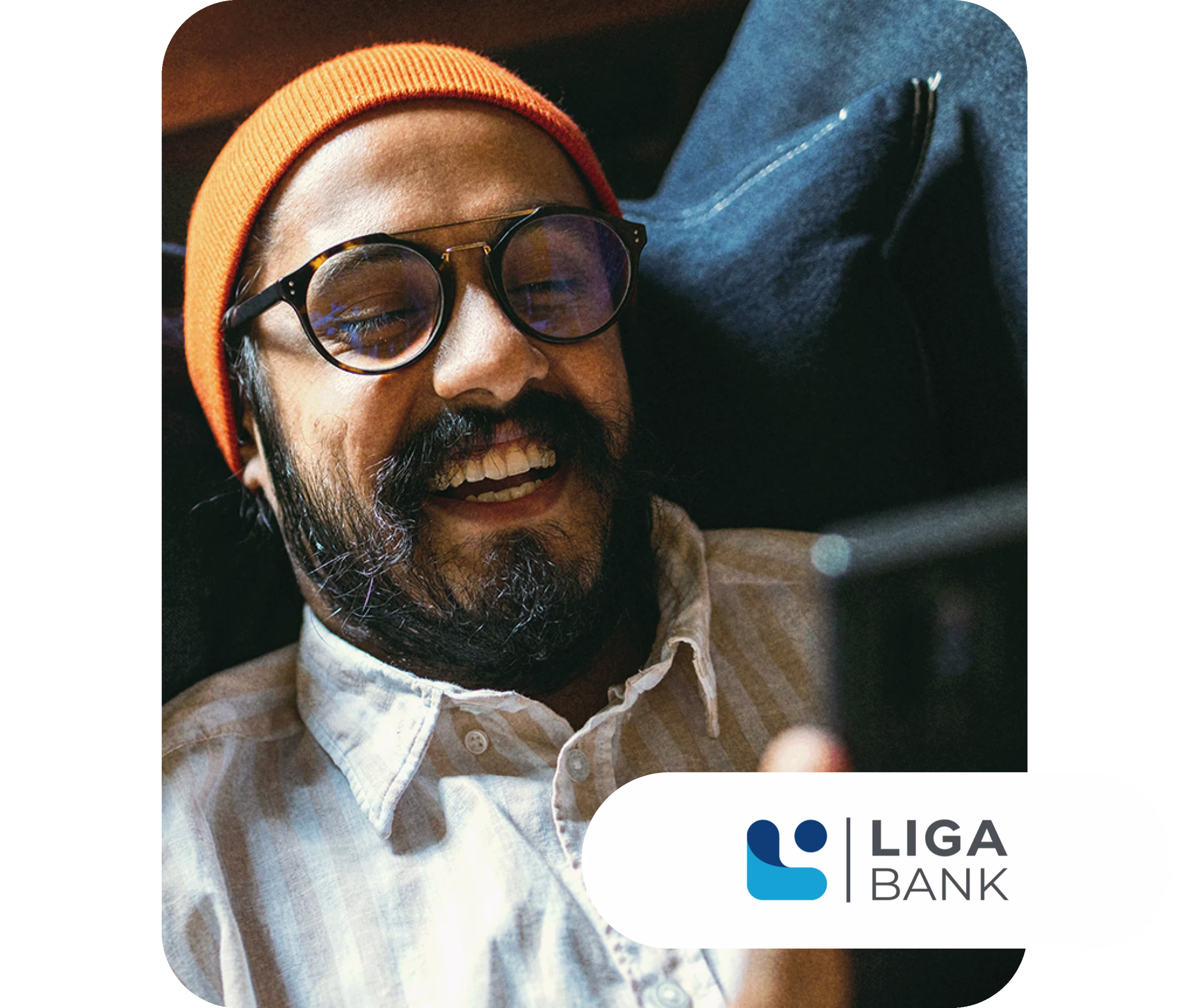Lächelnder Mann mit Brille und orangefarbener Mütze schaut auf sein Smartphone, im Hintergrund ein dunkler Polstersessel. Unten rechts ist das Logo der LIGA Bank zu sehen.
