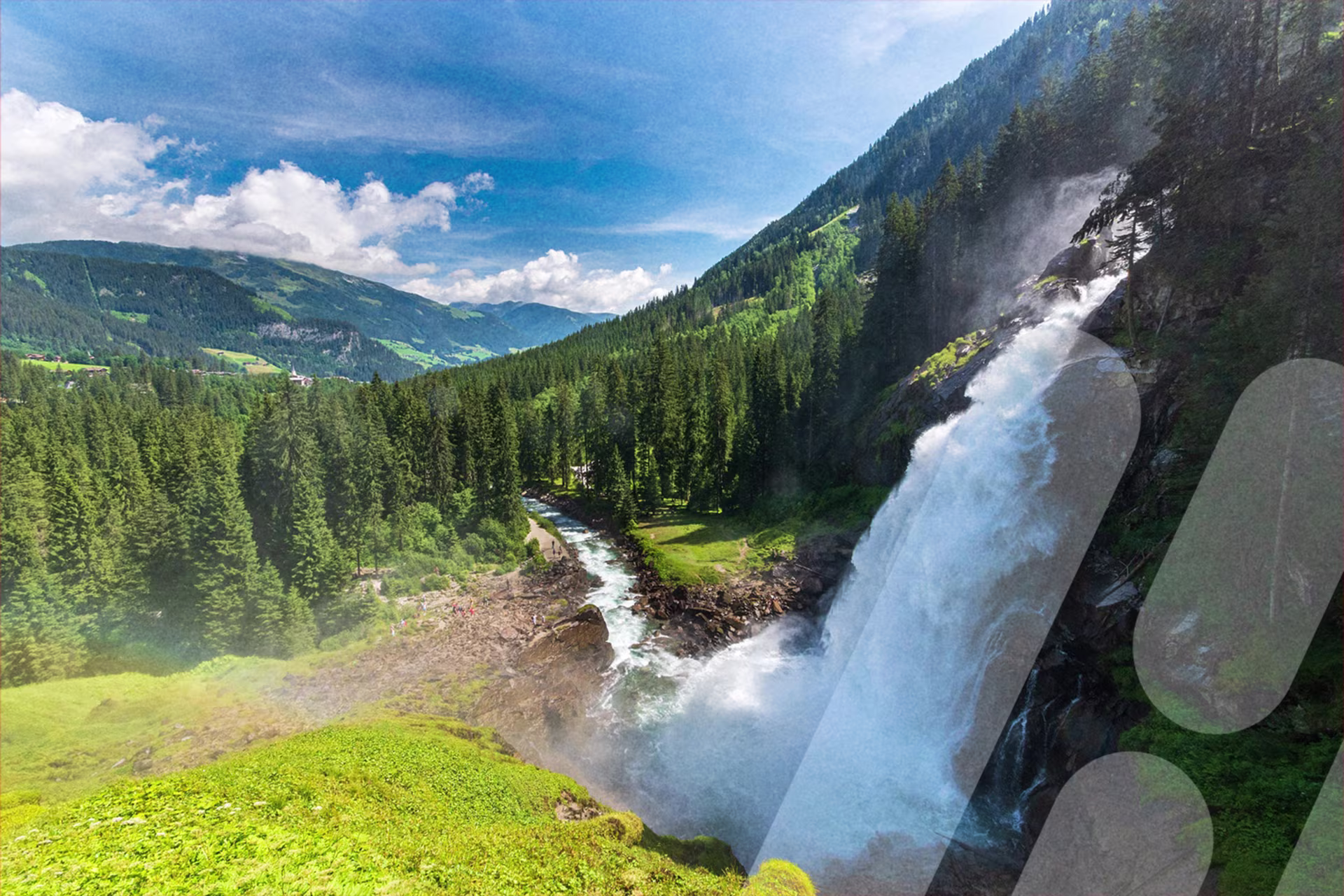 Großer Wasserfall stürzt einen bewaldeten Berghang hinab in einen Fluss. Umgeben von grünen Wiesen, dichten Nadelwäldern und Bergen unter blauem Himmel mit weißen Wolken.