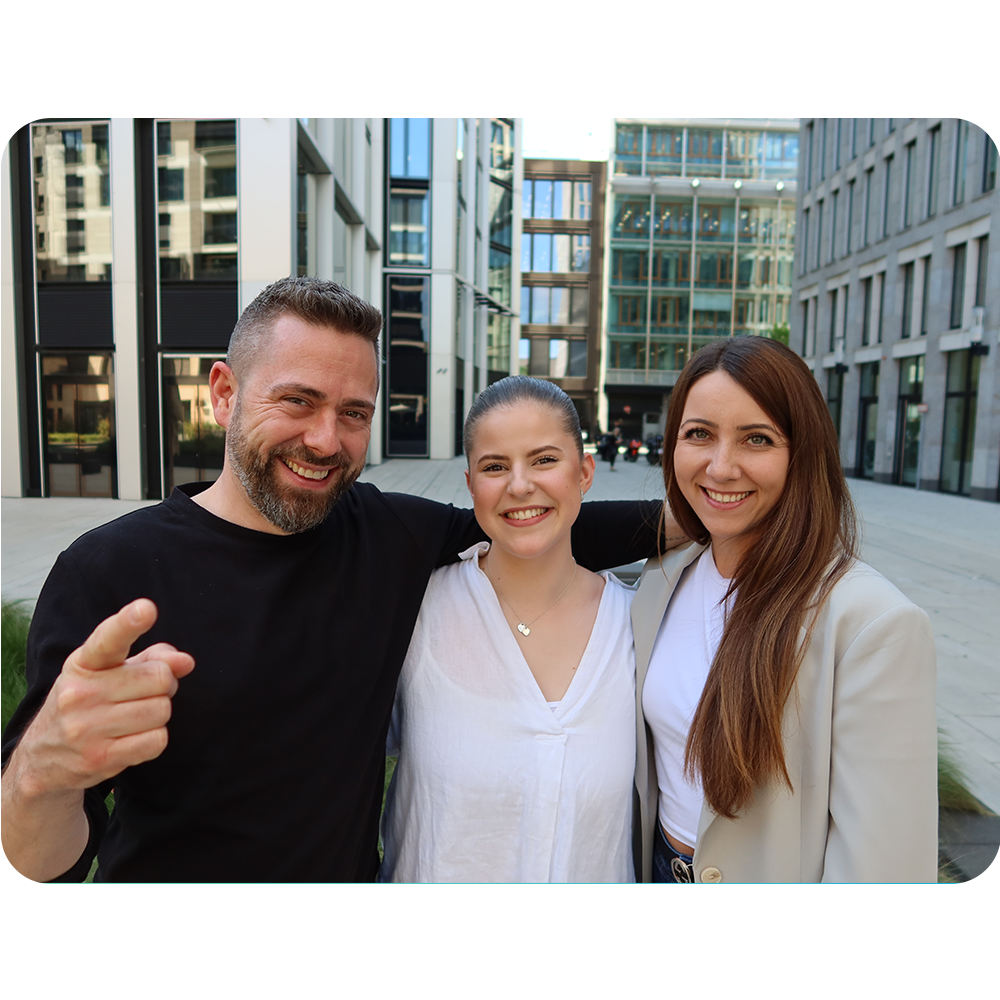 Drei Mitglieder des Nachhaltigkeitsteams von VisualVest – zwei Frauen und ein Mann – stehen beieinander lächelnd im Innenhof eines modernen Bürogebäudes. Sie wirken offen und sympathisch.