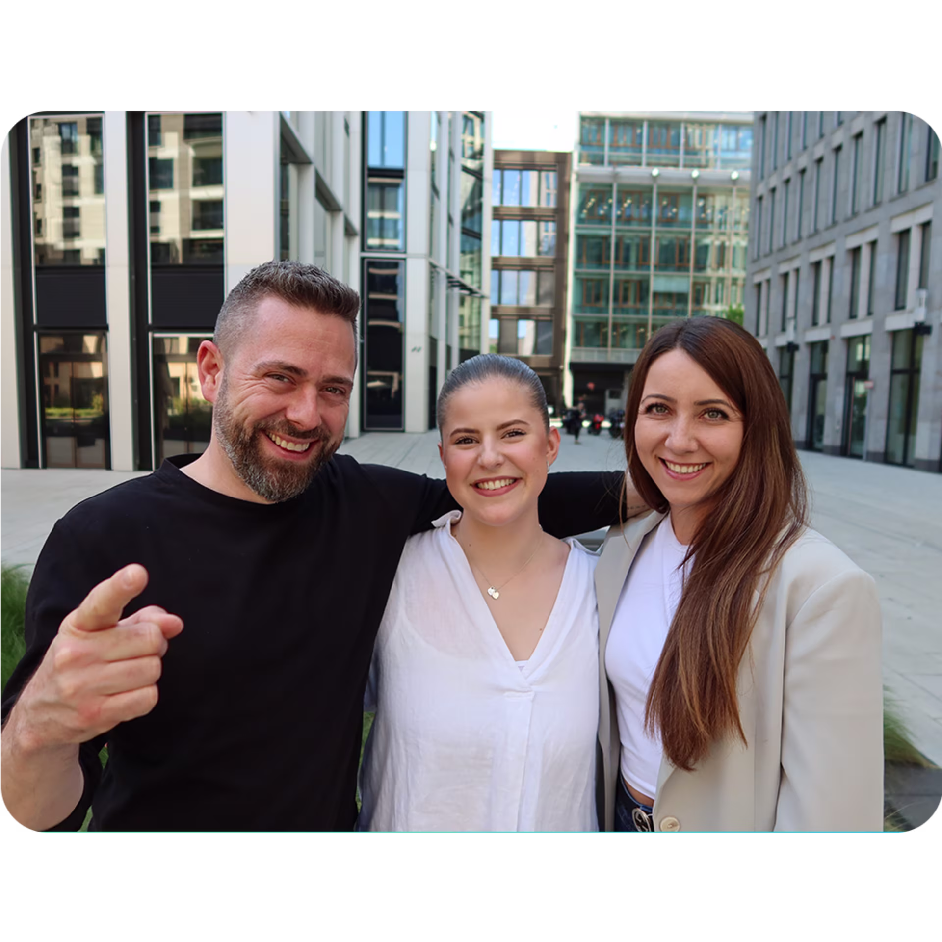 Drei Mitglieder des Nachhaltigkeitsteams von VisualVest – zwei Frauen und ein Mann – stehen beieinander lächelnd im Innenhof eines modernen Bürogebäudes. Sie wirken offen und sympathisch.