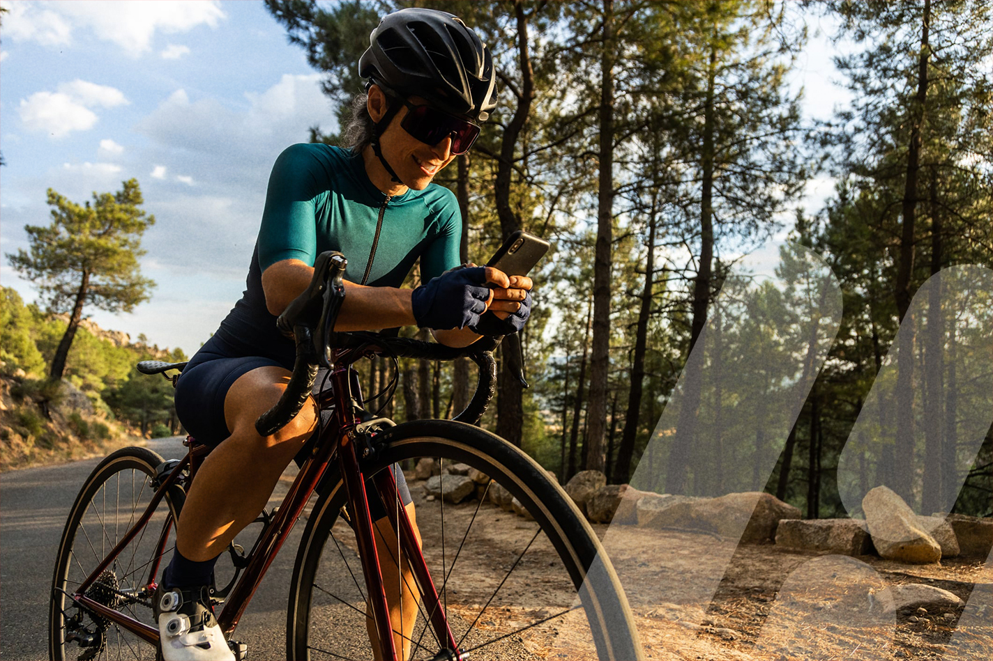 Eine Frau fährt steht mit ihrem Fahrrad im Wald und schaut aufs Handy