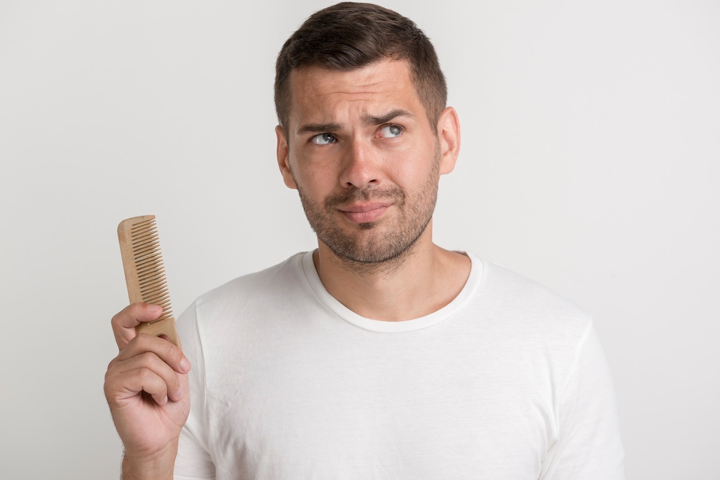 confused-young-man-holding-comb-looking-away-standing-against-white-wall 23-2148213328