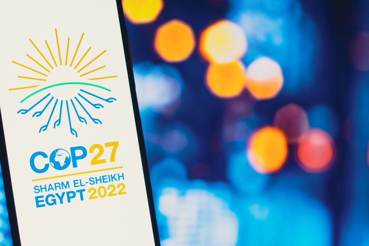 A mobile phone with the COP27 logo on it and bright lights in the background.