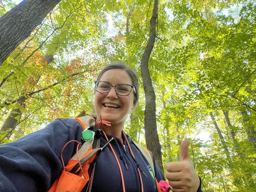 Chrissy Shaw outside in a forest smiling and giving the thumbs up.