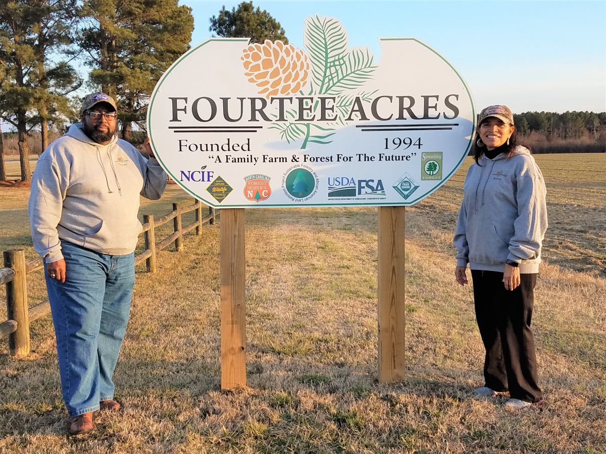 Two people standing on either side of an outdoor sign that says "Fourtee Acres Founded 1994."