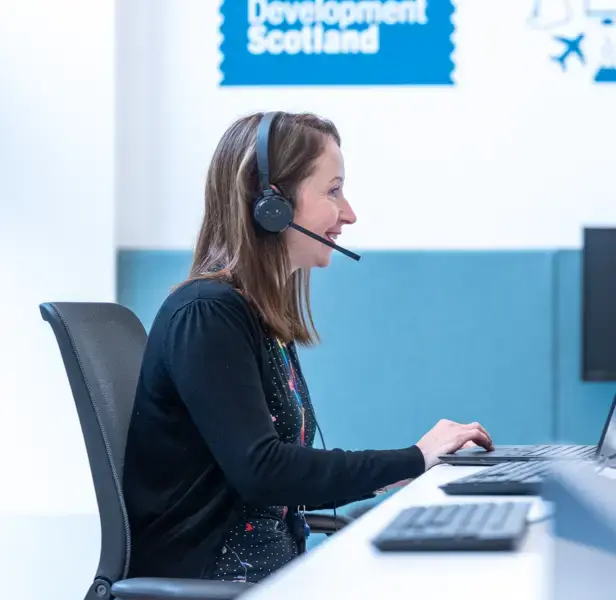 A woman using a computer and wearing a headset with a Skills Development Scotland sign in the background.