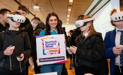 A woman holds a sign that says 'Scottish Careers Week'. Three pupils, who are wearing virtual reality headsets stand next to her.