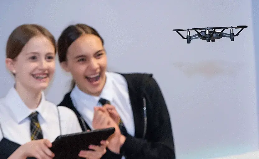 Two female school pupils smiling while flying a drone.
