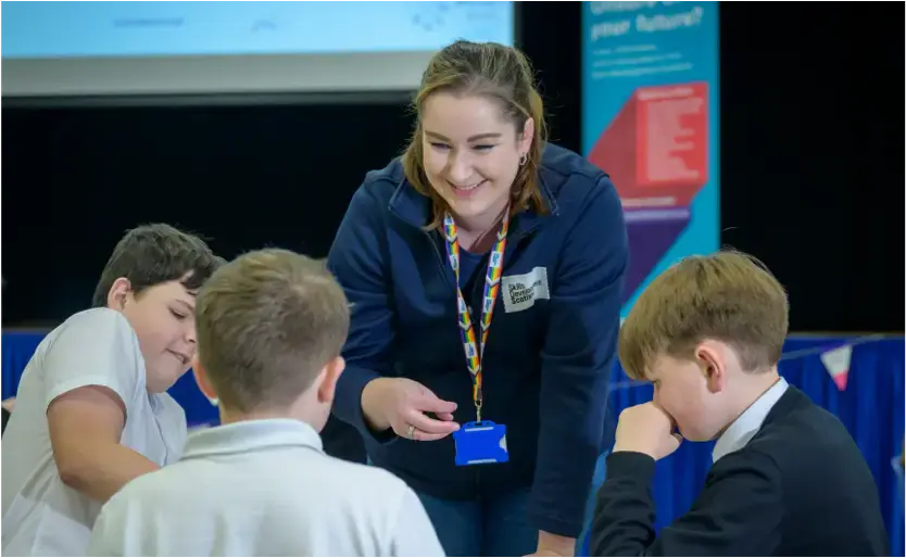 A woman wearing a Skills Development Scotland zipper and lanyard smiles as she stands next to three school pupils.