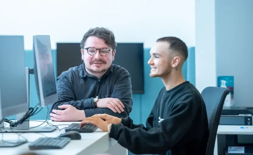 Smiling careers adviser talks to young man seated at computer