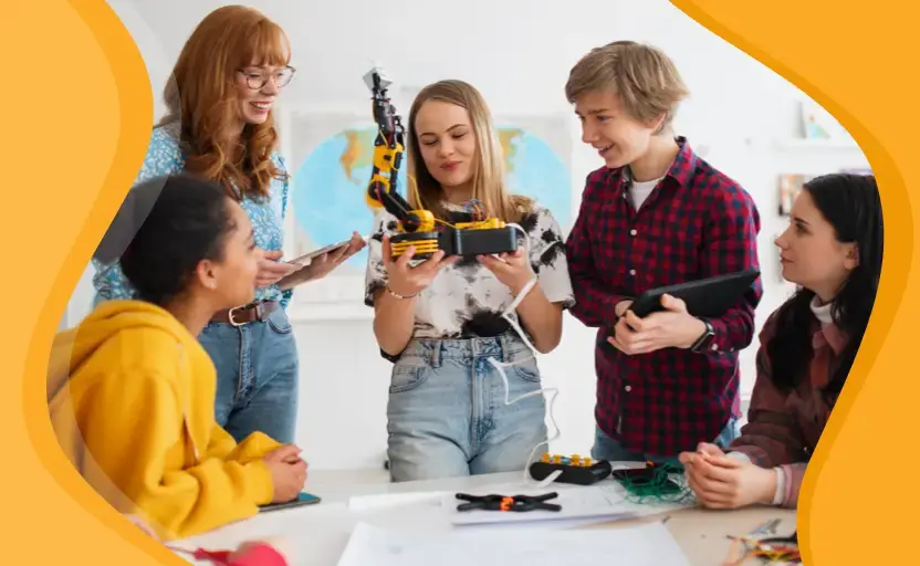 A group of young people in a classroom looking at and using a model of robotic arm. An expert is watching on.