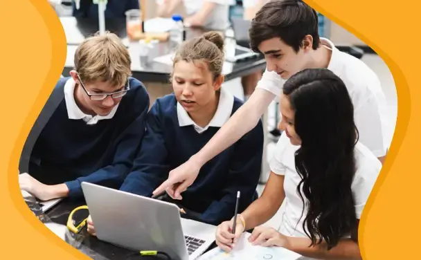 A group of school pupils sitting together around a laptop, discussing something they're working on.