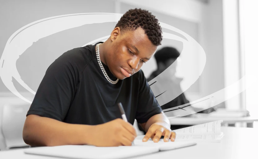 A young person sitting at a desk making notes in a notebook.