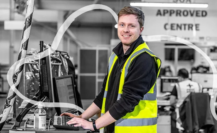 male engineer on computer smiling at camera wearing hi vis