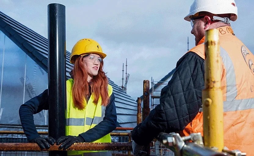 woman and man in high vis and safety hats looking at each other