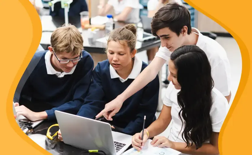 A group of school pupils sitting around a laptop, discussing something they're working together on.