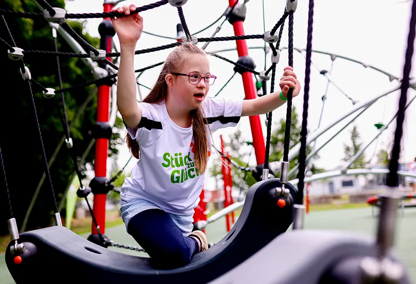 Ein Mädchen mit Downsyndrom klettert an einer Seil-Kletterstruktur auf einem inklusiven Klettergerüst
