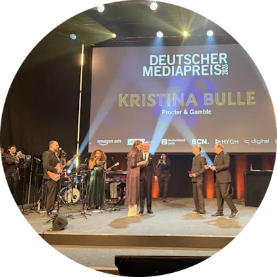 Bühnenaufnahme einer Preisverleihung mit Live‑Band und mehreren Personen auf der Bühne vor einer großen Leinwand, auf der ‚Deutscher Mediapreis 2023‘ und der Name ‚Kristina Bulle, Procter & Gamble‘ angezeigt werden.