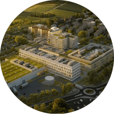 Luftaufnahme eines modernen Büro- und Campusgebäudekomplexes mit mehreren Gebäuden, Grünflächen, Straßen und einem Kreisverkehr in der Umgebung.