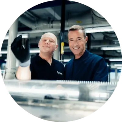 Foto von einem Gillette Mitarbeitenden und Kai Pflaume in einer Fabrikumgebung, wobei der Mann Kai eine Gillette Rasierklinge zeigt.
