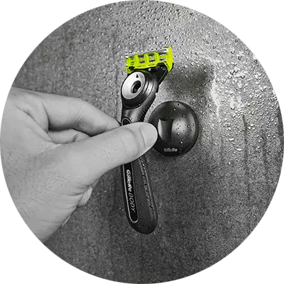 Hand setzt einen Rasierer auf eine wandmontierte Halterung in der Dusche, mit sichtbaren Wassertropfen auf der Oberfläche.