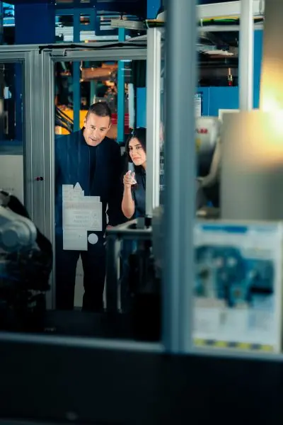 Foto von Kai und einer Fachkraft in einer Produktions- oder Industrieumgebung, die Maschinen oder Anlagen begutachten.