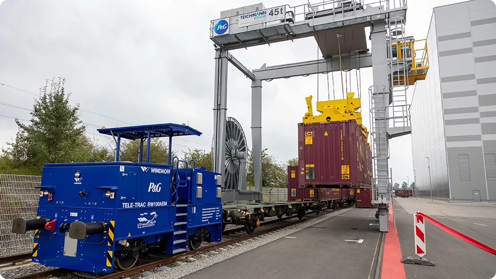 Ein Kran, der bei der dabei hilft, Container auf ein Gleis zu verladen.