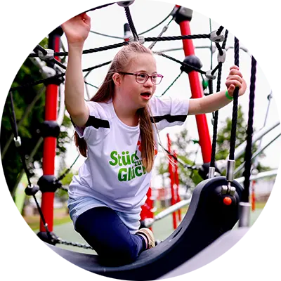 Ein Mädchen mit Downsyndrom klettert an einer Seil-Kletterstruktur auf einem inklusiven Klettergerüst
