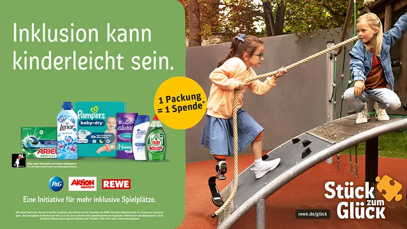 in Mädchen mit Beinprothese klettert an einem Seil eine Rampe auf einem inklusiven Spielplatz hoch, ein weiteres Mädchen schaut zu. Motiv zur Initiative „Stück zum Glück“ von P&G, Aktion Mensch und REWE für inklusive Spielplätze.
