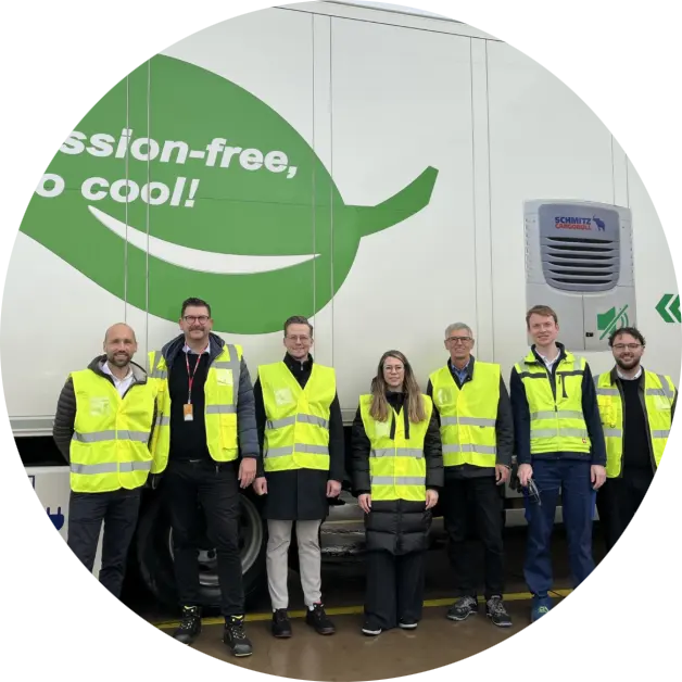 Gruppe von Mitarbeitenden in Warnwesten vor einem elektrisch betriebenen Kühlfahrzeug mit dem Slogan „Emission-free, so cool!“