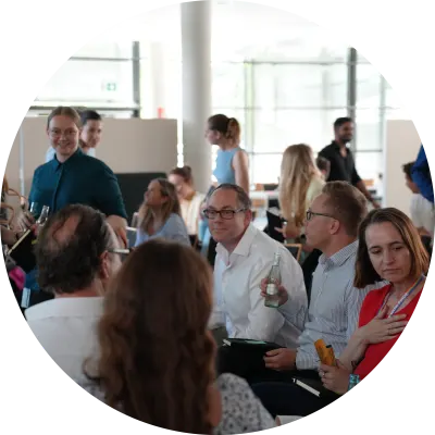 Mitarbeitende unterschiedlichen Alters in einem hellen Raum, die sich in kleinen Teams unterhalten und vernetzen.