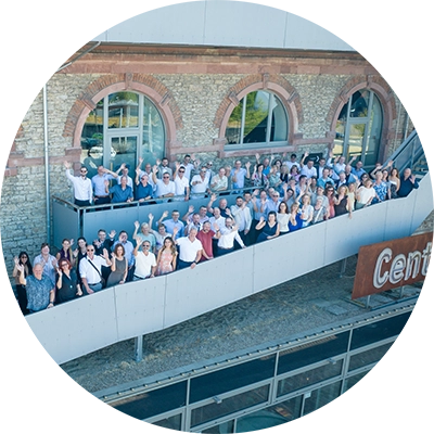 Große Gruppe von Mitarbeitenden auf einer Außenterrasse vor einem Firmengebäude, aufgenommen für ein Gruppenfoto.