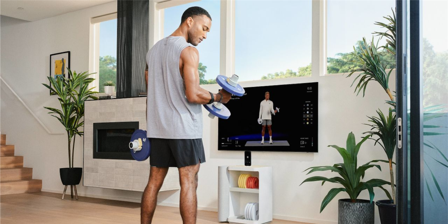 Athletic young man curling Tempo dumbbell while watching an instructor on his TV.