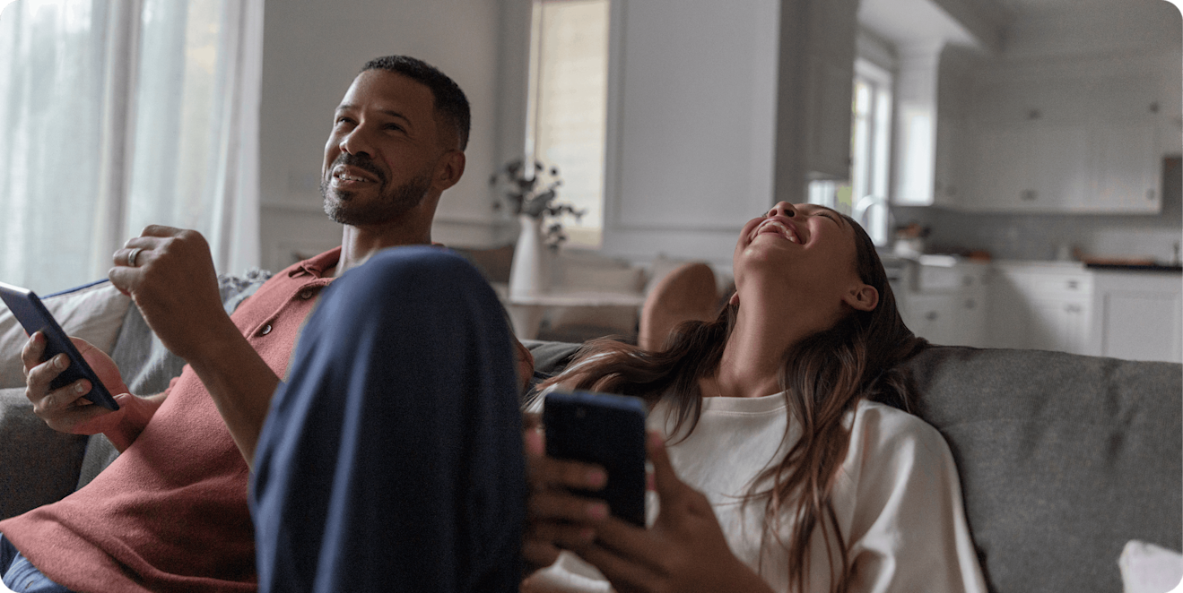 Two young adults relaxing and smiling while browsing on their smartphones, representing the ease and accessibility of managing payments with Affirm.